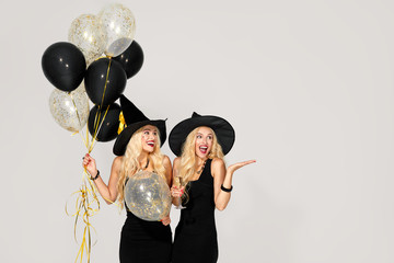 portrait of two happy young women in black witch halloween costumes with balloons on party over white background. the concept of Halloween . funny faces