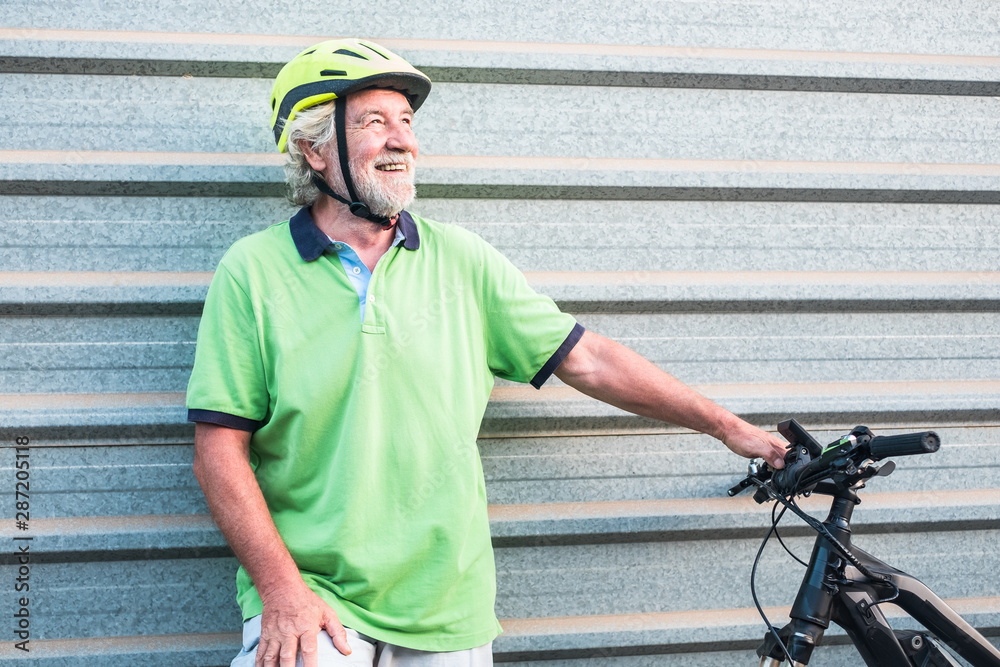 Senior people grandfather standing close to his e bike. Healthy lifestyle for retired person. Yellow helmet. Metal wall in background