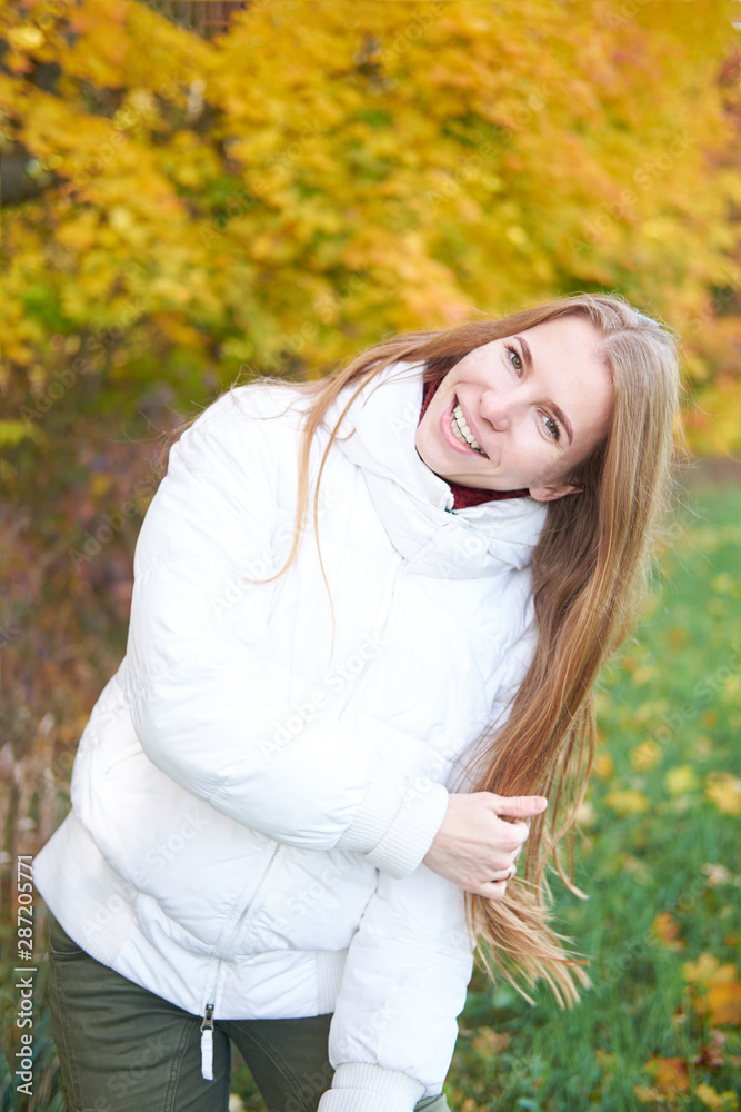 Portrait of young attractive cheerful girl with beautiful natural long hair wearing white jacket and green pants. Yellow autumn trees on background. Autumn time. Portrait of young attractive cheerful girl with beautiful natural long hair wearing white jacket and green pants. Yellow autumn trees on background. Autumn time.