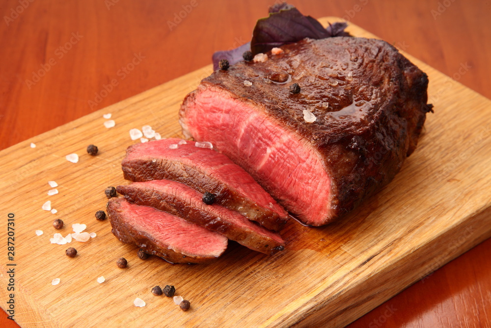 marbled beef steak, cut into pieces and served on an oak board, seasoned with Himalayan salt, black pepper and basil