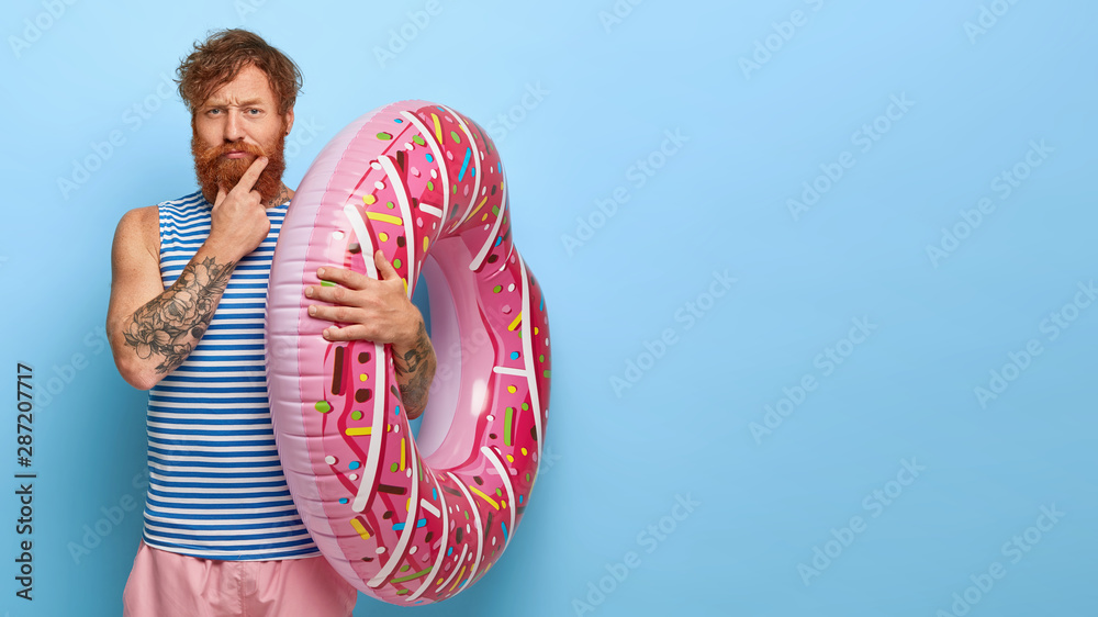 Photo of serious bearded adult ginger man holds big inflated swimring ...