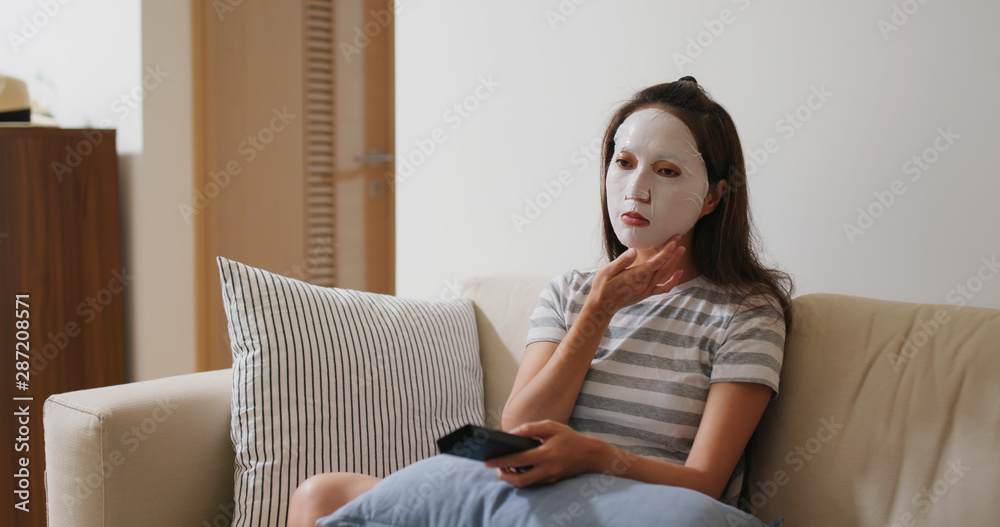 Woman apply face mask and watch tv at home Woman apply face mask and watch tv at home