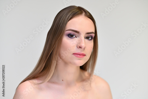 A close-up portrait of a cute girl, a young woman with beautiful curly hair on a white background with excellent face skin and outstanding fashionable make-up. Beauty, brightness.