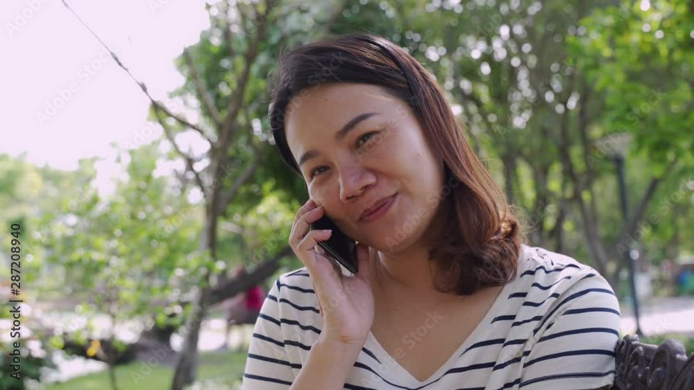 Woman in casual dress picking the smartphone to talking with friends on smiley face in the park. Woman in casual dress picking the smartphone to talking with friends on smiley face in the park.
