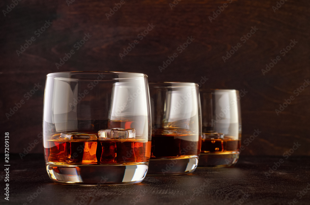 Glass of whiskey on a wooden tableThree glasses of whiskey with ice on the wooden table