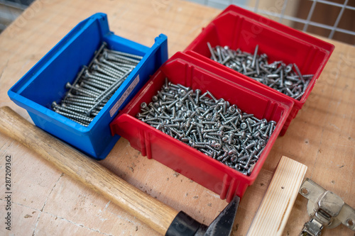 on the table are different coloured boxes filled with screws and next to them is a hammer