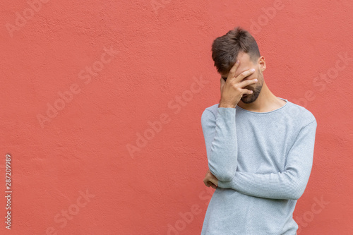 Stressed disappointed young guy making facepalm gesture with hand. Red wall background, copy space. Facepalm concept. photo