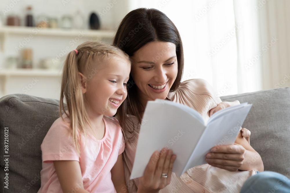 Cheerful mother and daughter sitting on couch reading fairytale Cheerful mother and daughter sitting on couch reading fairytale