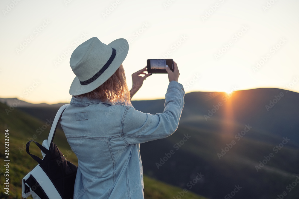 Obraz premium Young girl with a phone camera in the mountains during sunset. Girl and phone. Photographing landscapes by phone. Travel - Image