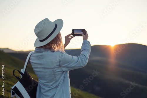 Young girl with a phone camera in the mountains during sunset. Girl and phone. Photographing landscapes by phone. Travel - Image