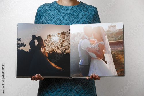 woman holds open family photobook. the person looks at the photo book turn.  beige sample  photo album . wedding photoalbum with  fabric cover .female hands holding square open photo album. photo