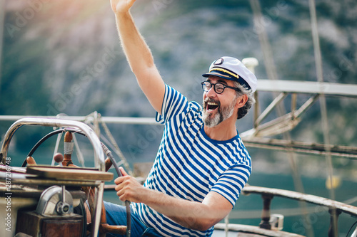 Mature man standing at helm of sailboat out at sea on a sunny afternoon. © Mediteraneo