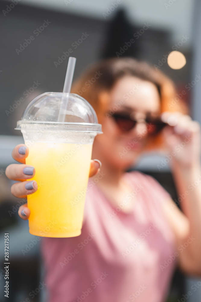 08.12.2018 Vinnitsa, Ukraine: photo of a bright yellow cocktail in a transparent plastic glass holding a girl with red hair in her hand, her face blurred 08.12.2018 Vinnitsa, Ukraine: photo of a bright yellow cocktail in a transparent plastic glass holding a girl with red hair in her hand, her face blurred