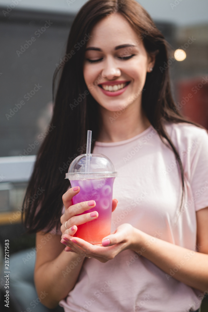 pretty and attractive woman holding a plastic glass with a cold multicolored summer cocktail with a good smile and cheerful mood