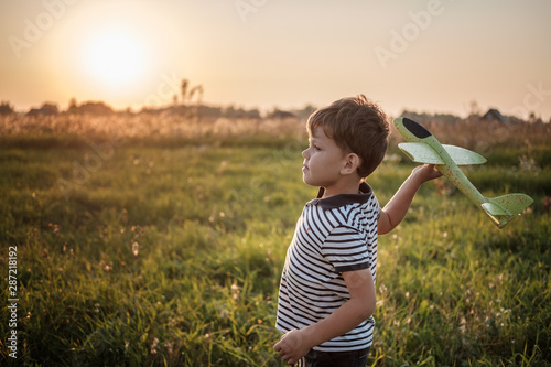 Schilderij op canvas cute boy playing airplane on a summer evening against the sunset