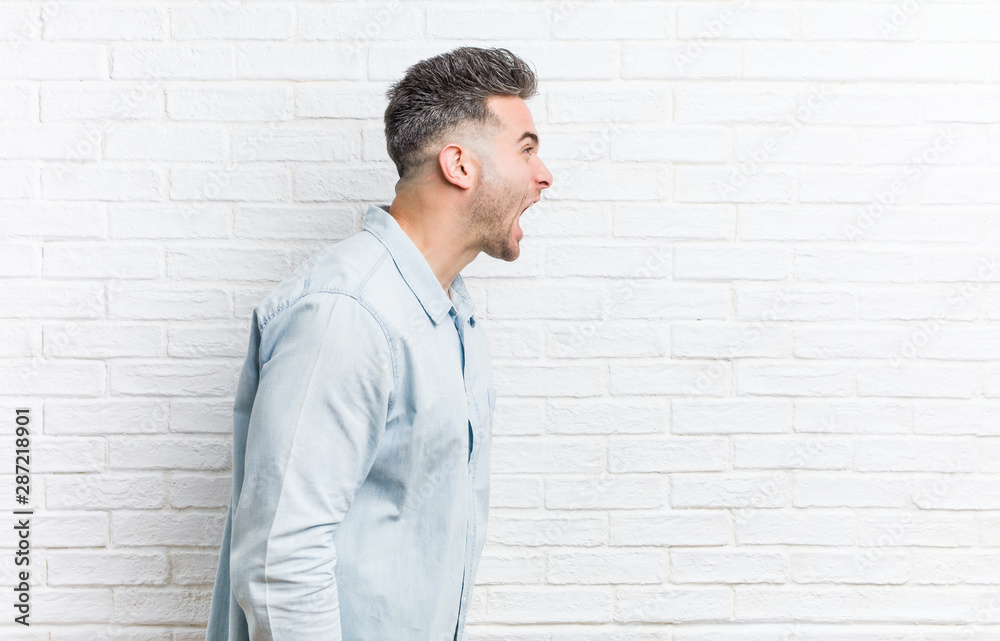 Young handsome man against a bricks wall shouting towards a copy space Young handsome man against a bricks wall shouting towards a copy space