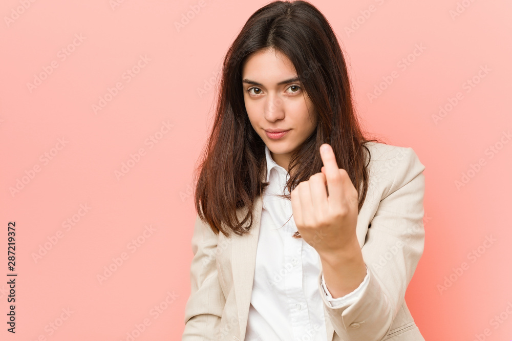 Young brunette business woman against a pink background pointing with finger at you as if inviting come closer. Young brunette business woman against a pink background pointing with finger at you as if inviting come closer.