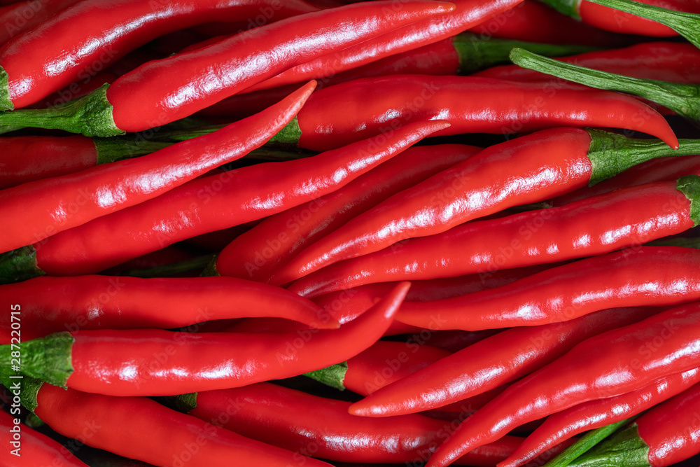 Red hot chili pepper background. Flat lay. Red ripe peppers with green stems, top view. Spicy seasoning close up. Food background.