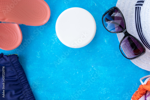 Summer vacation concept, accessories for summer travel flay lay on light blue background with a hat, sunscrin care cream and phone with copy space for text