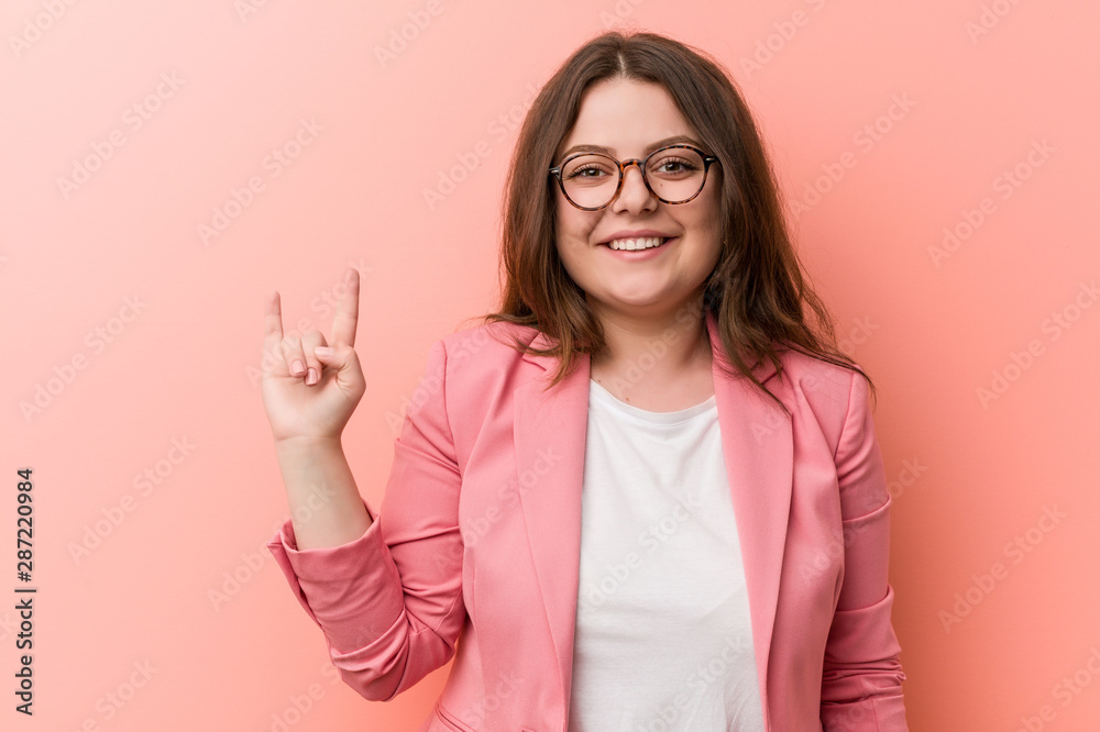 Young plus size business caucasian woman showing a horns gesture as a revolution concept.