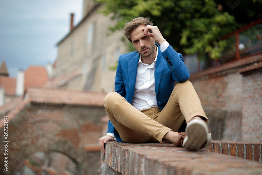 Fototapeta premium pensive fashion man sitting on brick wall and rests