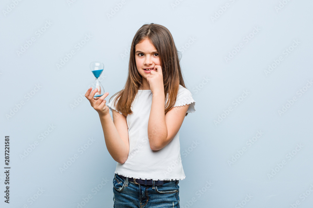 Little caucasian girl holding an hourglass relaxed thinking about something looking at a copy space. Little caucasian girl holding an hourglass relaxed thinking about something looking at a copy space.