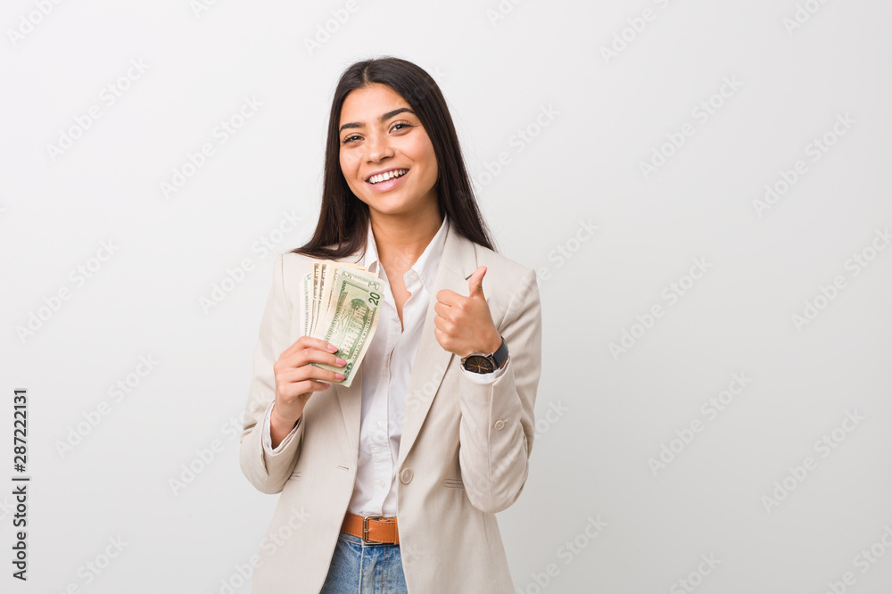 Young arab business woman holding dollars smiling and raising thumb up Young arab business woman holding dollars smiling and raising thumb up
