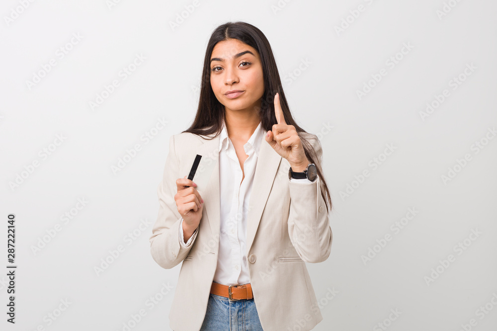 Young arab woman holding a credit card showing number one with finger. Young arab woman holding a credit card showing number one with finger.
