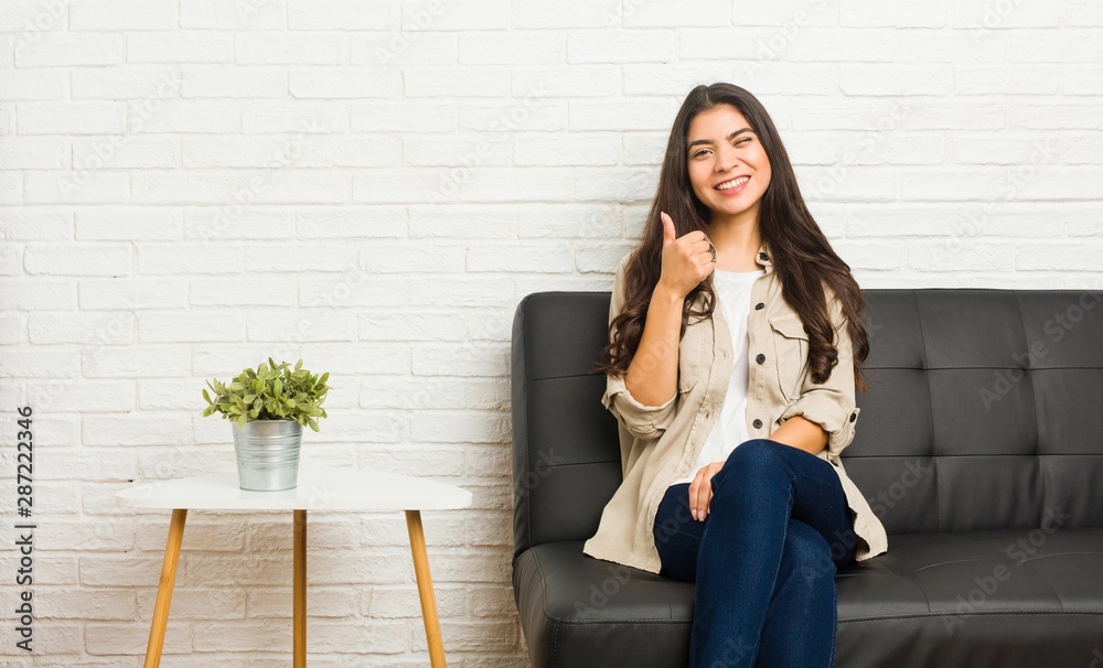 Young arab woman sitting on the sofa smiling and raising thumb up Young arab woman sitting on the sofa smiling and raising thumb up