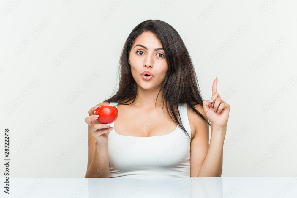 Young hispanic woman holding a tomato having some great idea, concept of creativity. Young hispanic woman holding a tomato having some great idea, concept of creativity.