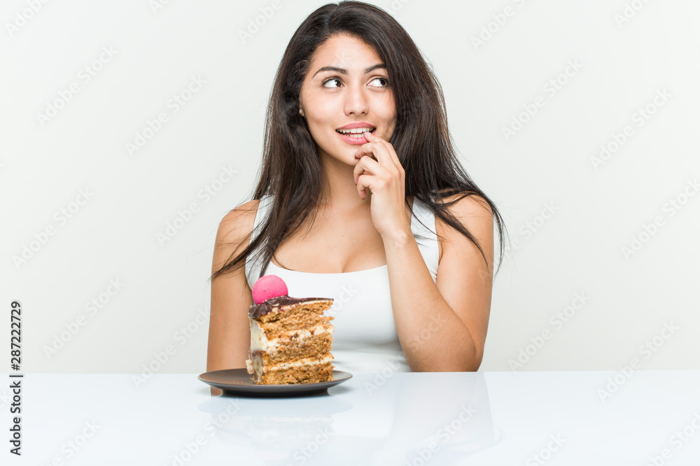 Young hispanic woman eating a cake relaxed thinking about something looking at a copy space. Young hispanic woman eating a cake relaxed thinking about something looking at a copy space.