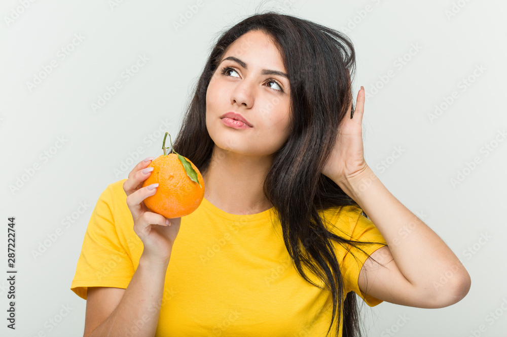 Young hispanic woman holding an orange trying to listening a gossip. Young hispanic woman holding an orange trying to listening a gossip.