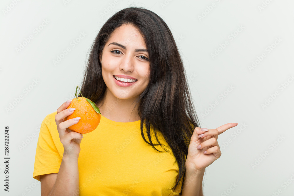 Young hispanic woman holding an orange smiling cheerfully pointing with forefinger away. Young hispanic woman holding an orange smiling cheerfully pointing with forefinger away.