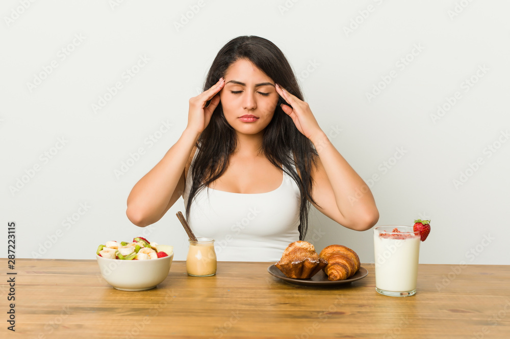 Young curvy woman taking a breakfast touching temples and having headache. Young curvy woman taking a breakfast touching temples and having headache.