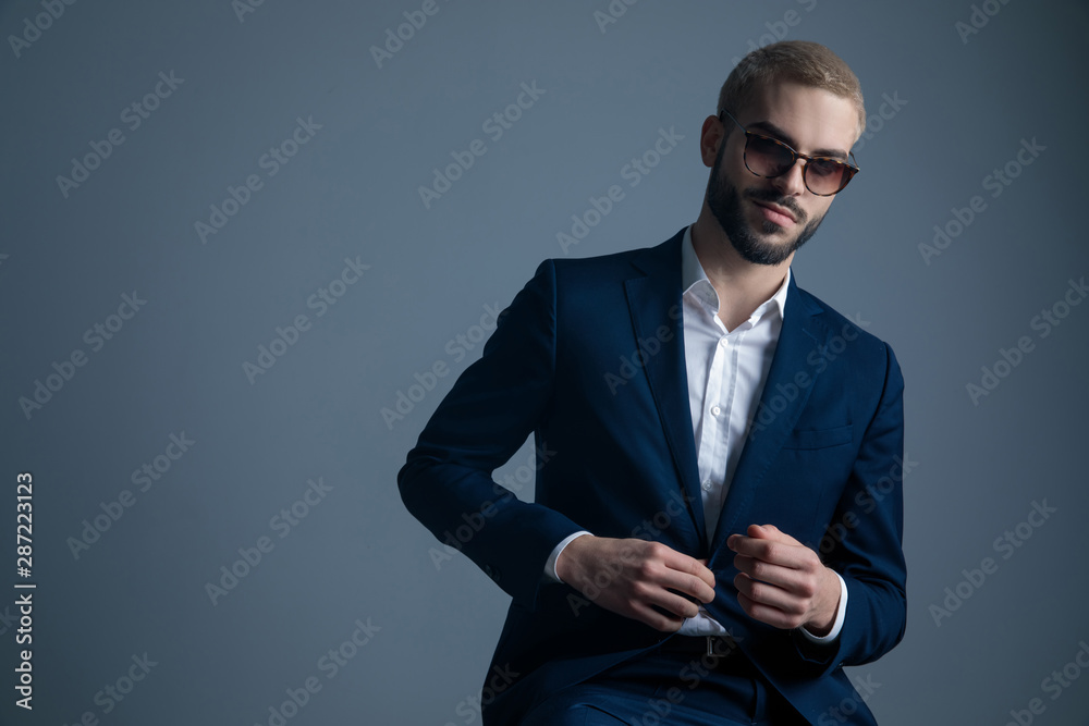 cool guy in sunglasses buttoning his suit and smiles