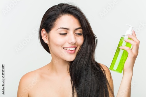 Close up of a young beautiful and natural hispanic woman holding an aloe vera bottle