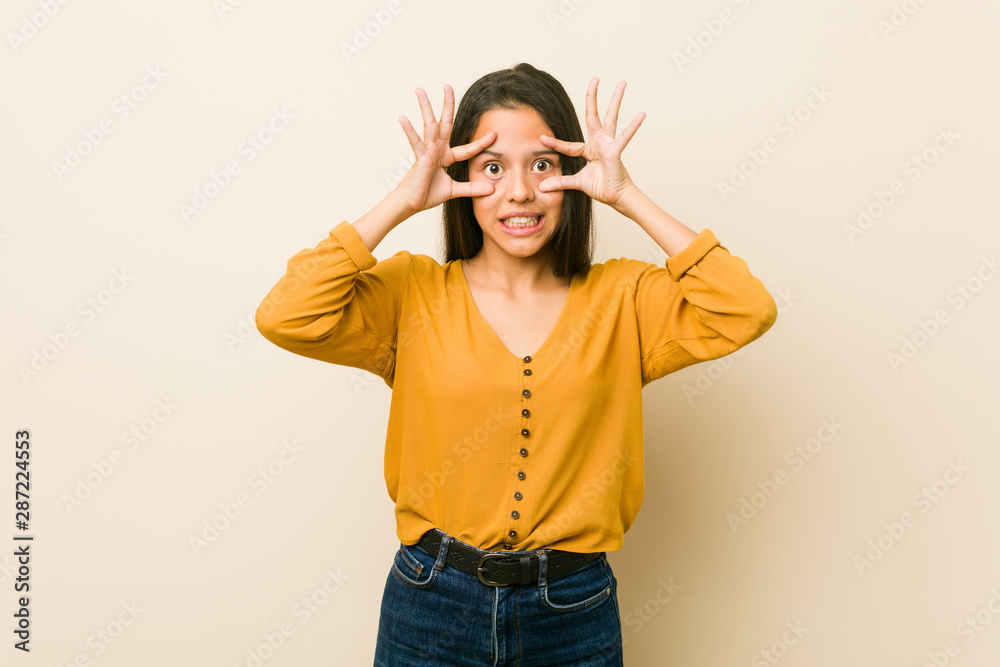 Young hispanic woman against a beige background keeping eyes opened to find a success opportunity. Young hispanic woman against a beige background keeping eyes opened to find a success opportunity.