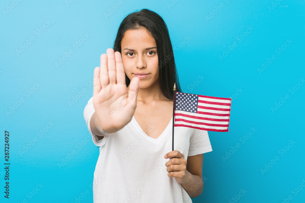 Young hispanic woman holding a united states flag standing with outstretched hand showing stop sign, preventing you. Young hispanic woman holding a united states flag standing with outstretched hand showing stop sign, preventing you.