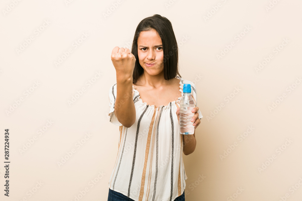 Young hispanic woman holding a bottle of water showing fist to camera, aggressive facial expression. Young hispanic woman holding a bottle of water showing fist to camera, aggressive facial expression.