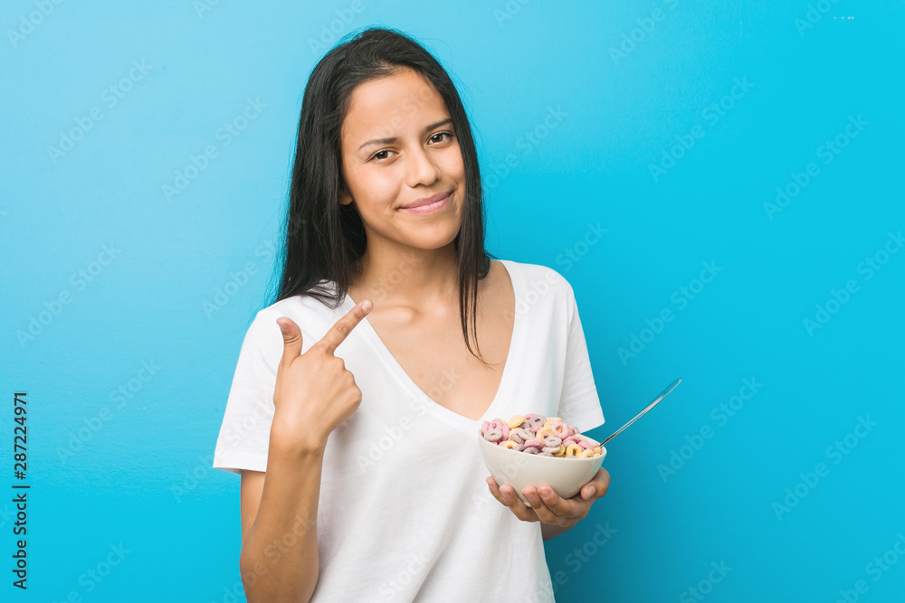 Young hispanic woman holding a sugar cereal bowl pointing with finger at you as if inviting come closer. Young hispanic woman holding a sugar cereal bowl pointing with finger at you as if inviting come closer.