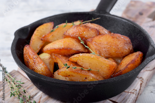 Golden roasted potato wedges in a cast iron pan on white wooden table