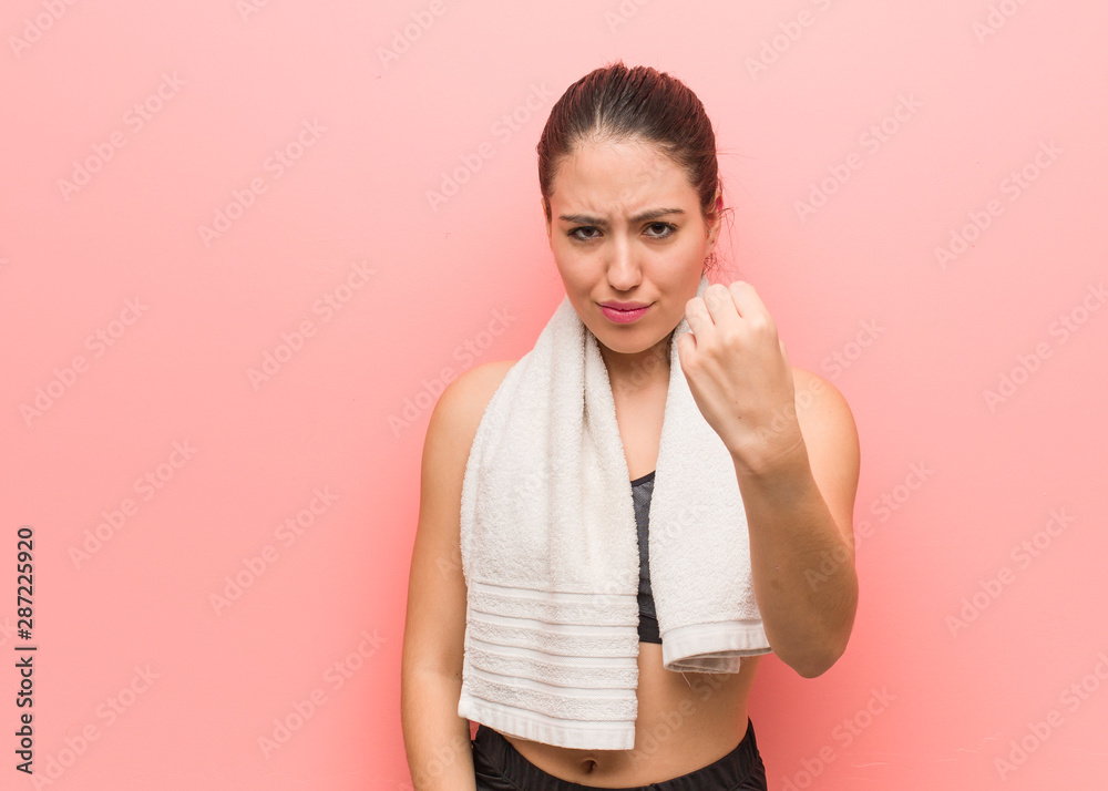 Young fitness woman showing fist to front, angry expression