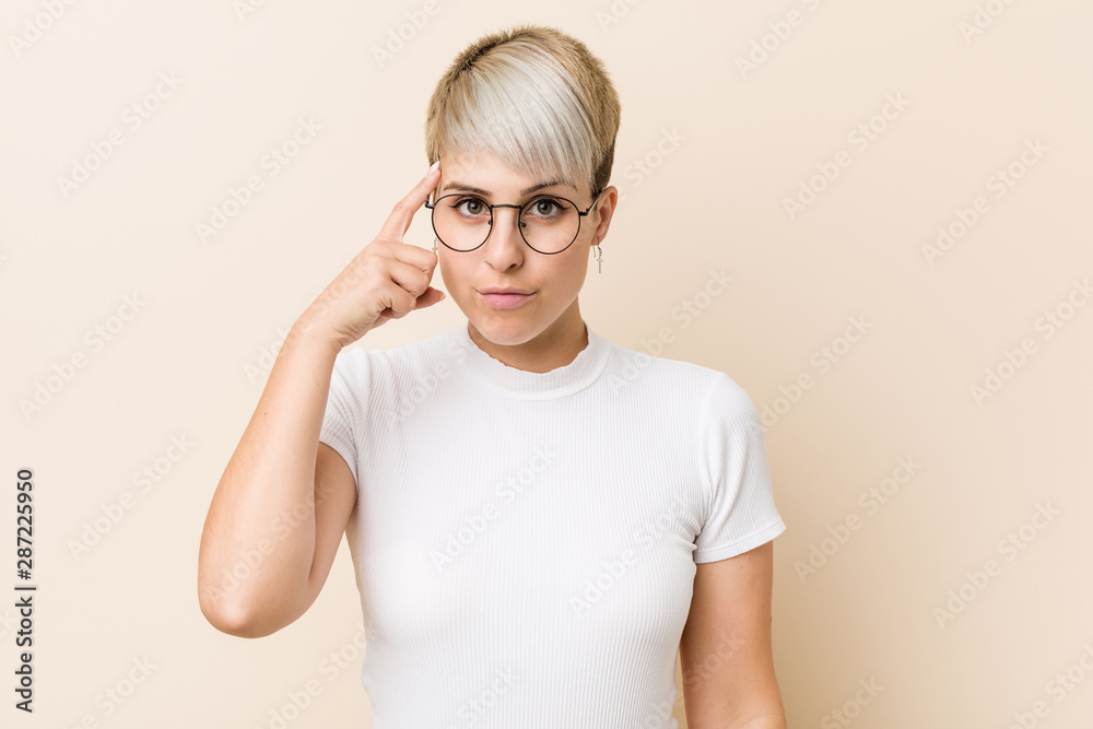 Young authentic natural woman wearing a white shirt pointing temple with finger, thinking, focused on a task. Young authentic natural woman wearing a white shirt pointing temple with finger, thinking, focused on a task.