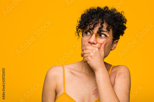 Young african american woman with skin birth mark thoughtful looking to a copy space covering mouth with hand.