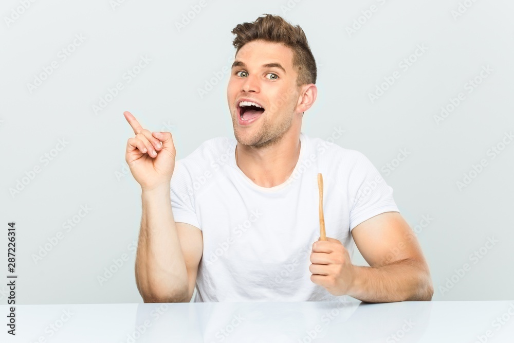Young man holding a toothbrush smiling cheerfully pointing with forefinger away. Young man holding a toothbrush smiling cheerfully pointing with forefinger away.