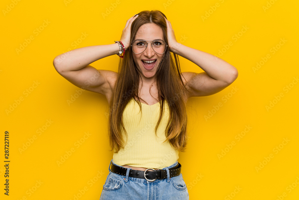 Young redhead ginger woman with freckless laughs joyfully keeping hands on head. Happiness concept. Young redhead ginger woman with freckless laughs joyfully keeping hands on head. Happiness concept.