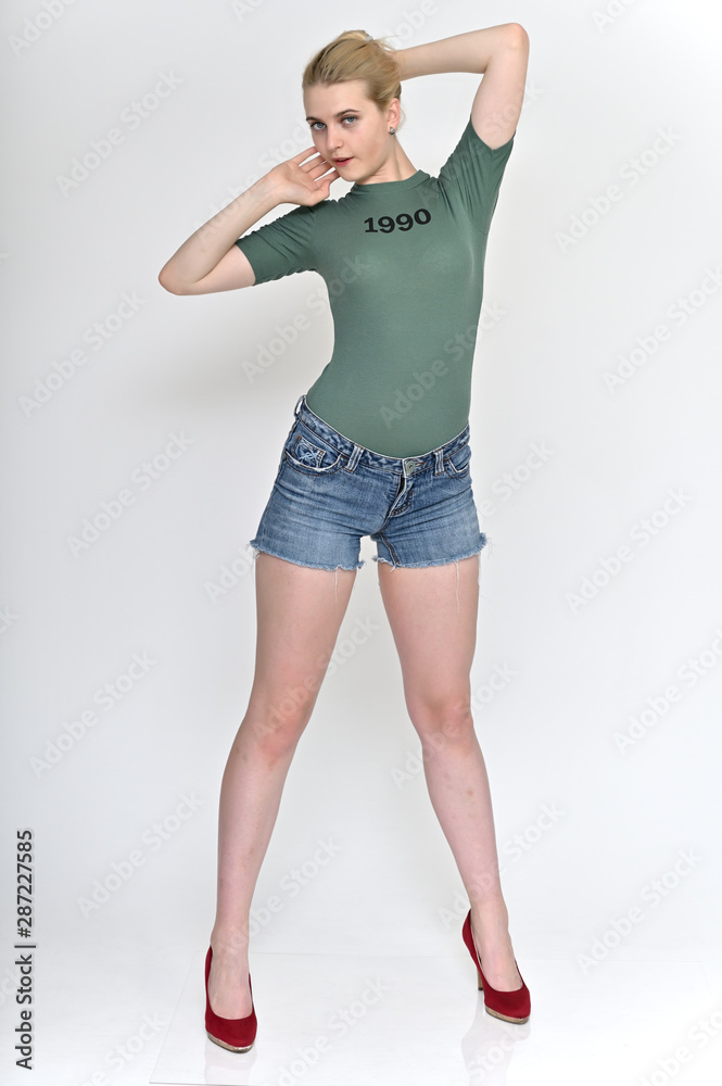 Full length vertical Portrait of a cute blonde student girl, a young woman in a green T-shirt and blue shorts with beautiful curly hair on a white background in various poses. Full length vertical Portrait of a cute blonde student girl, a young woman in a green T-shirt and blue shorts with beautiful curly hair on a white background in various poses.