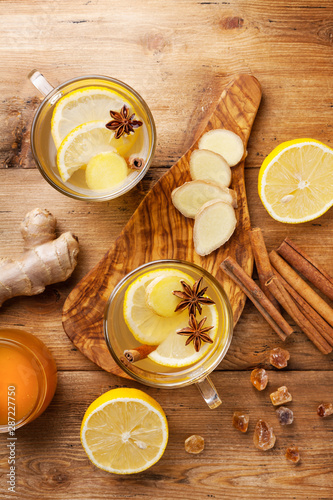 Healing ginger tea in two glass mug with lemon, honey and spices. Autumn hot drink on rustic wooden table top view.