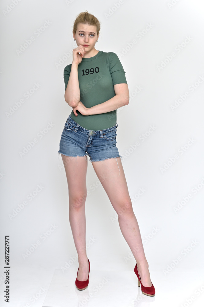 Full length vertical Portrait of a cute blonde student girl, a young woman in a green T-shirt and blue shorts with beautiful curly hair on a white background in various poses. Full length vertical Portrait of a cute blonde student girl, a young woman in a green T-shirt and blue shorts with beautiful curly hair on a white background in various poses.