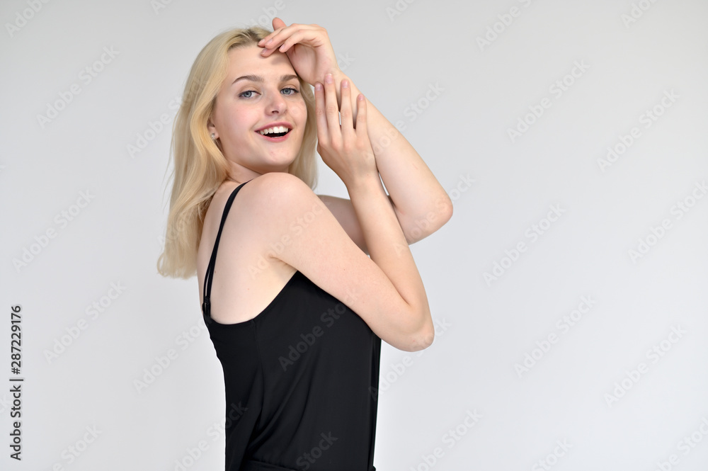 Portrait of a cute blonde student girl, a young woman in a black dress with beautiful curly hair on a white background in different poses. Shows hands to the sides. Beauty, brightness, emotions. Portrait of a cute blonde student girl, a young woman in a black dress with beautiful curly hair on a white background in different poses. Shows hands to the sides. Beauty, brightness, emotions.